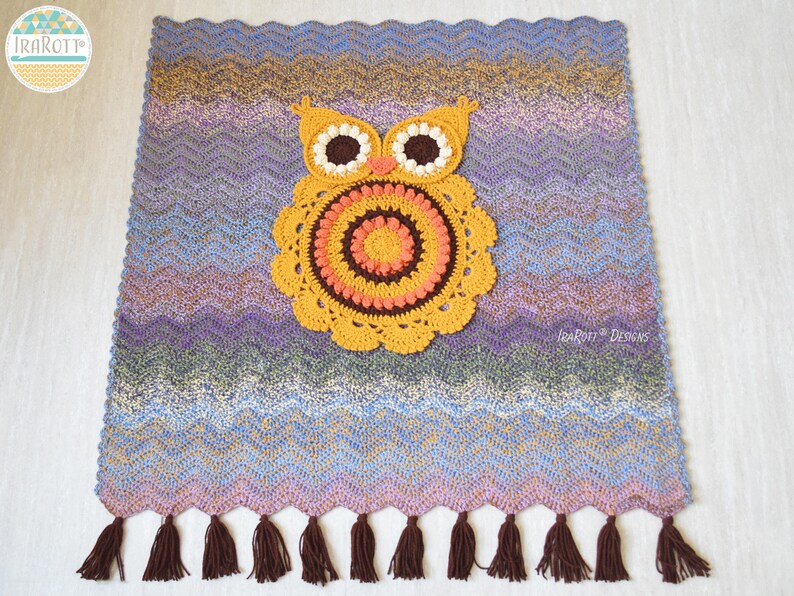 May include: A handmade crochet owl-themed blanket with a chevron pattern in shades of blue, purple, and brown. The owl is yellow, orange, and brown. The blanket has a fringe of brown tassels along the bottom. The blanket is approximately 30 inches wide and 30 inches long.