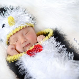 Op de afbeelding: Een pasgeboren baby draagt een zwart-wit pinguïn kostuum met een gele snavel en een rode strik. Het kostüm is gemaakt van pluche garen en heeft een muts met een zwart-wit pinguïn gezicht.