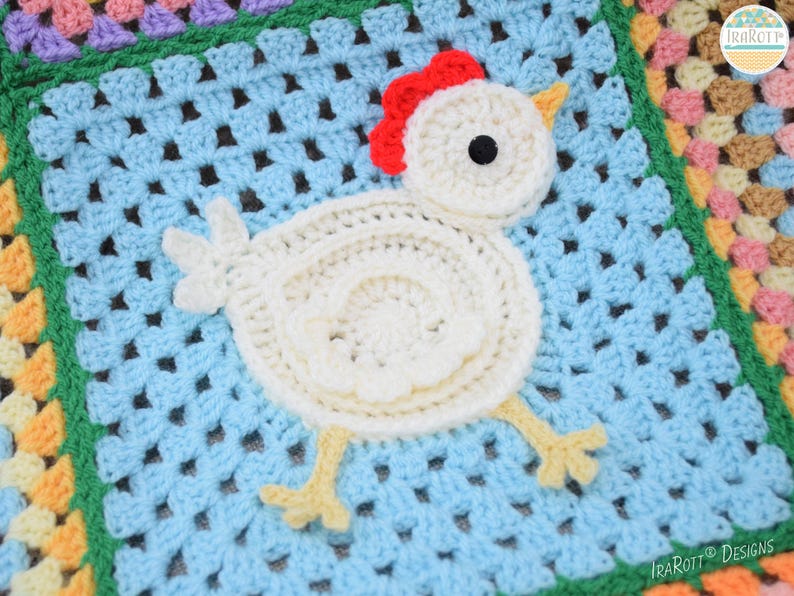 Pode incluir: Um cobertor de croch&ecirc; de quadrados da av&oacute; com uma aplica&ccedil;&atilde;o de frango de croch&ecirc; branco no centro. O frango tem uma crista vermelha, olhos pretos e p&eacute;s amarelos.
