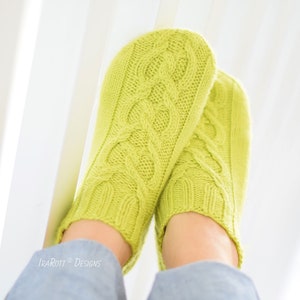May include: A pair of lime green knitted socks with a cable knit pattern. The socks are worn by a person sitting on a white chair.
