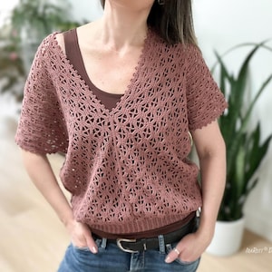 Puede incluir: Top de ganchillo rosa empolvado con cuello en V y mangas cortas. El top tiene un patrón abierto y calado y se lleva sobre una camiseta sin mangas marrón. La modelo lleva vaqueros azules y un cinturón negro. Es una prenda hecha a mano.