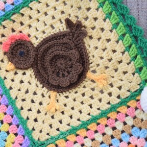 Pode incluir: Um cobertor de beb&eacute; de croch&ecirc; com um design de patchwork colorido. O cobertor apresenta uma aplica&ccedil;&atilde;o de frango de croch&ecirc; castanho com um ovo de croch&ecirc; branco.
