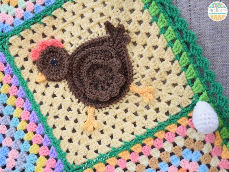 Pode incluir: Um cobertor de beb&eacute; de croch&ecirc; com um design de patchwork colorido. O cobertor apresenta uma aplica&ccedil;&atilde;o de frango de croch&ecirc; castanho com um ovo de croch&ecirc; branco.