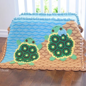 Puede incluir: Una manta de bebé de ganchillo con una escena de océano azul y marrón. Dos tortugas verdes y amarillas aparecen en la manta. La manta tiene un borde festoneado.