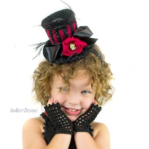 Puede incluir: Una niña pequeña con un sombrero de copa de crochet negro y rojo con un lazo negro y una flor roja con un diseño de calavera. También lleva guantes sin dedos de crochet negro.