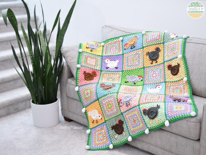Pode incluir: Uma manta de croch&ecirc; colorida com um design de patchwork que apresenta quadrados de v&aacute;rias cores e galinhas aplicadas. A manta &eacute; decorada com pompons brancos ao redor das bordas.