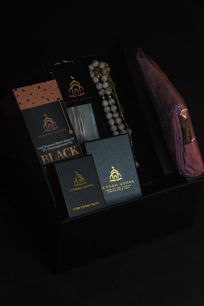 May include: A black gift box containing various items. Included are boxes of black seed oil and pure thimid oil, a beaded rosary, and a wrapped pink scarf. The boxes have the text "SUNNAH GOODS".