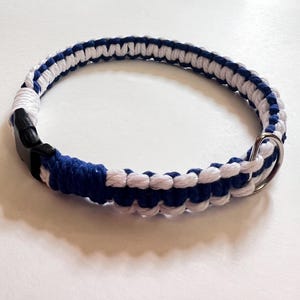 以下が含まれることがあります： 黒いプラスチック製のバックルとシルバーの金属リングが付いた、青と白の編み込み犬用首輪。 首輪は厚くて耐久性のある素材でできており、犬の首の周りに着用するように設計されています。