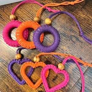 May include: Three crocheted heart-shaped ornaments and three crocheted circle ornaments with wooden beads and strings. The ornaments are in shades of pink, orange, and purple.