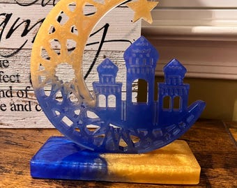 May include: A blue and gold resin sculpture of a crescent moon with a star and a mosque. The sculpture is on a blue and gold base.