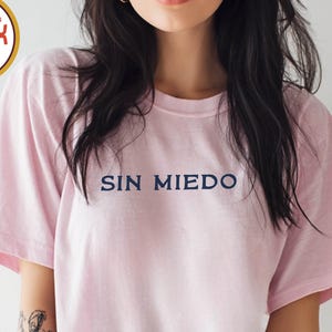 Könnte beinhalten: Hellrosa Unisex-T-Shirt mit dem navyblauen Schriftzug "SIN MIEDO". Das Shirt besteht aus 100 % Baumwolle und ist in den Größen S-4XL erhältlich. Es trägt außerdem die Aufschriften "ORIGINAL" und "COMFORT COLORS Premium Quality".