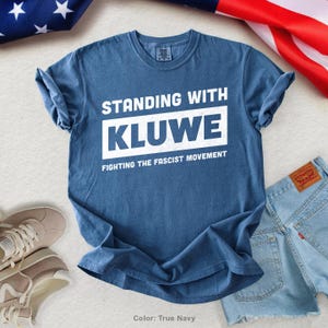 May include: A blue t-shirt with white text that reads "Standing with Kluwe Fighting the Fascist Movement".