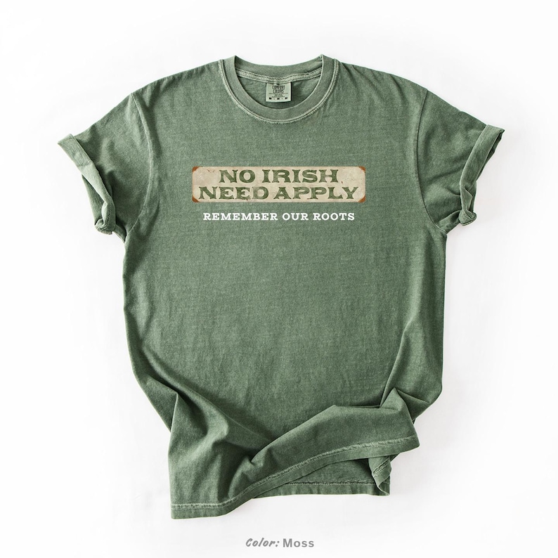Graphic tee featuring the phrase “No Irish Need Apply” with “Remember Our Roots” printed beneath in bold white lettering. A vintage, historical design on a Comfort Colors® cotton shirt, perfect for Irish Americans, history buffs, educators, and those honoring immigrant heritage. Ideal for St. Patrick’s Day, cultural pride, or anti-discrimination messaging. Available in unisex sizing.