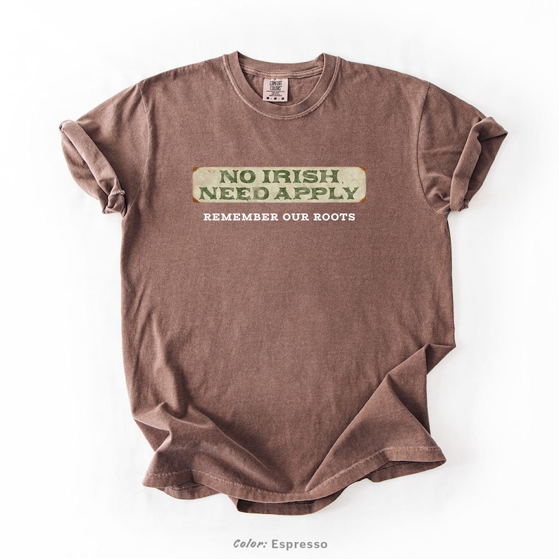 Graphic tee featuring the phrase “No Irish Need Apply” with “Remember Our Roots” printed beneath in bold white lettering. A vintage, historical design on a Comfort Colors® cotton shirt, perfect for Irish Americans, history buffs, educators, and those honoring immigrant heritage. Ideal for St. Patrick’s Day, cultural pride, or anti-discrimination messaging. Available in unisex sizing.