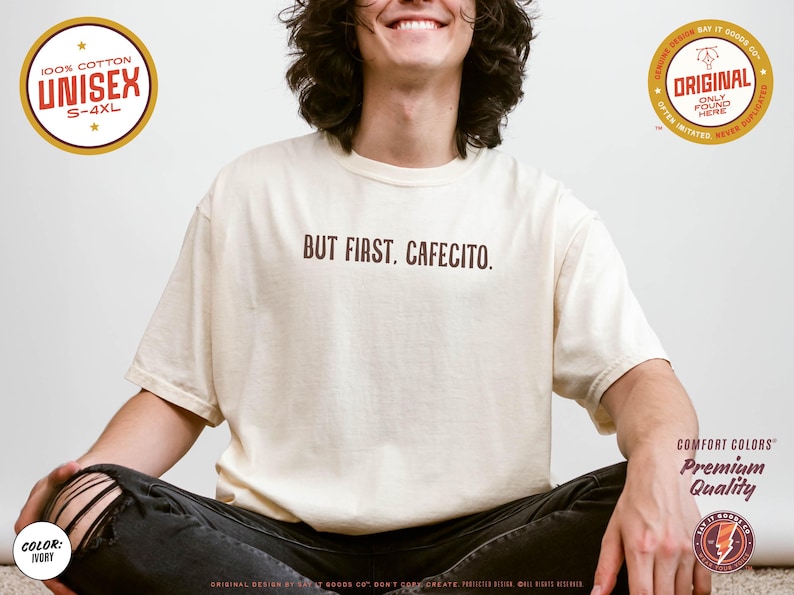K&ouml;nnte beinhalten: Beigefarbenes Unisex-T-Shirt mit dem braunen Schriftzug "BUT FIRST, CAFECITO.". Das Shirt besteht aus 100 % Baumwolle und ist in den Gr&ouml;&szlig;en S-4XL erh&auml;ltlich. Das Bild enth&auml;lt auch Design-Details und Branding-Elemente.