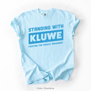 May include: Light blue t-shirt with the text "Standing with Kluwe Fighting the Fascist Movement" in blue.