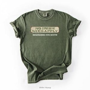Graphic tee featuring the phrase “No Irish Need Apply” with “Remember Our Roots” printed beneath in bold white lettering. A vintage, historical design on a Comfort Colors® cotton shirt, perfect for Irish Americans, history buffs, educators, and those honoring immigrant heritage. Ideal for St. Patrick’s Day, cultural pride, or anti-discrimination messaging. Available in unisex sizing.