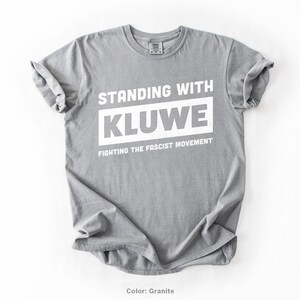 May include: A gray t-shirt with the text "Standing with Kluwe Fighting the Fascist Movement" printed in white.