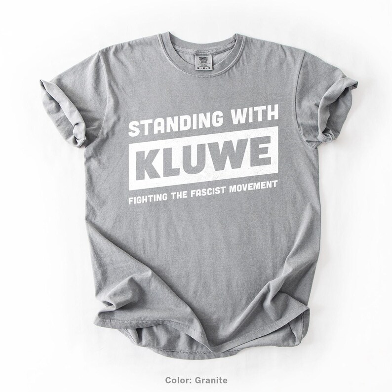 May include: A gray t-shirt with the text "Standing with Kluwe Fighting the Fascist Movement" printed in white.