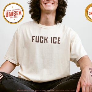 May include: Ivory-colored unisex t-shirt with the text "FUCK ICE" in brown block letters. The shirt is made of 100% cotton and is available in sizes S-4XL. Additional circular logos indicate the shirt's original design and premium quality.