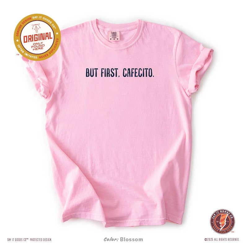 K&ouml;nnte beinhalten: Hellrosa T-Shirt mit dem marineblauen Aufdruck "BUT FIRST, CAFECITO.". Das Shirt hat kurze &Auml;rmel und einen Rundhalsausschnitt. Die Farbe wird als "Blossom" bezeichnet.