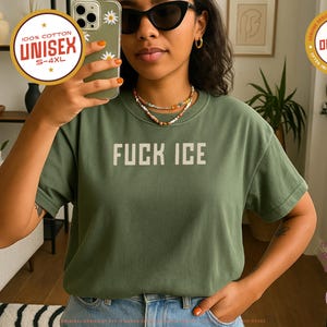 May include: Moss green unisex t-shirt with the text "FUCK ICE" in white block letters. The shirt is 100% cotton and available in sizes S-4XL. A round sticker indicates the design is original.