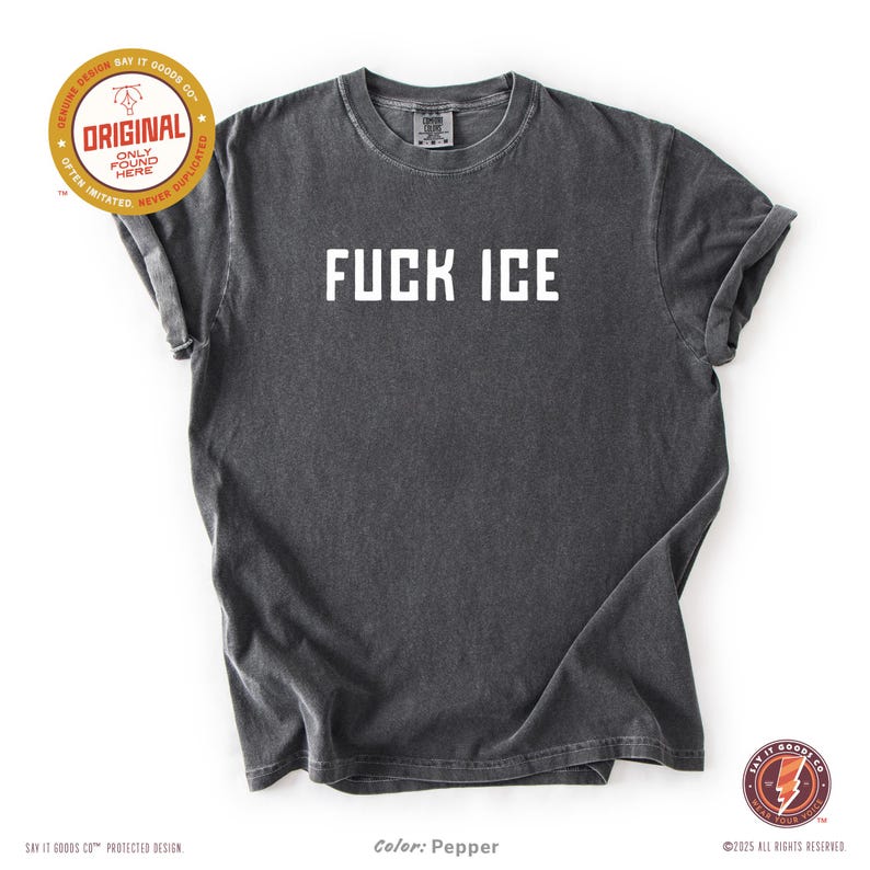 May include: A dark gray t-shirt with the text "FUCK ICE" in white block letters. The shirt has a vintage, worn look. The image includes the text "ORIGINAL" and "SAY IT GOODS CO" in a circular design.