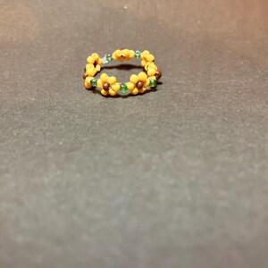 Puede incluir: Un anillo de cuentas amarillas y verdes con un diseño de girasol.