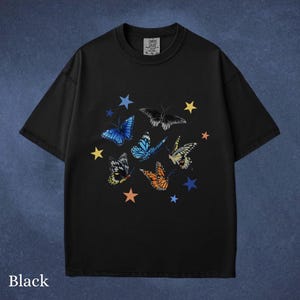 May include: Black t-shirt featuring a colorful butterfly and star design. The butterflies are in shades of blue, orange, yellow, and black. The text "Black" is at the bottom of the shirt.