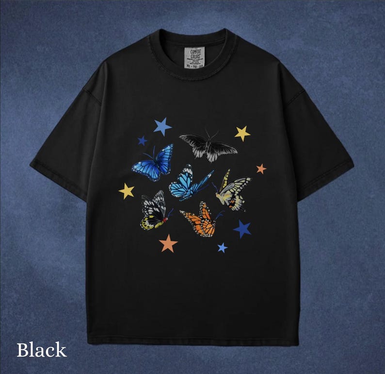 May include: Black t-shirt featuring a colorful butterfly and star design. The butterflies are in shades of blue, orange, yellow, and black. The text "Black" is at the bottom of the shirt.