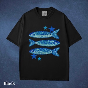 May include: Black t-shirt featuring three blue fish and blue stars. The fish have a textured design. The shirt has a crew neck and short sleeves. The word "Black" is at the bottom of the shirt.