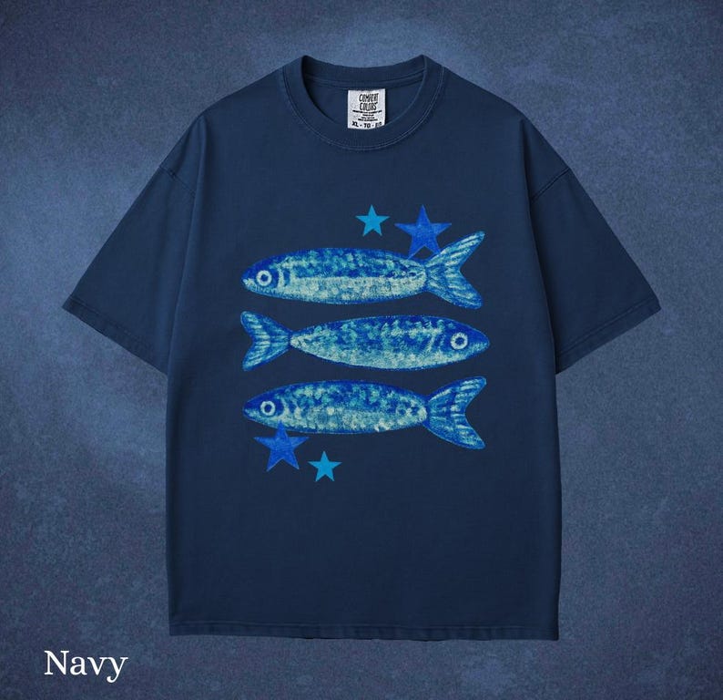 May include: Navy blue t-shirt featuring a design of three blue fish and blue stars. The shirt has a crew neck and short sleeves. The text "Comfort Cruise" is printed on the upper right of the shirt.