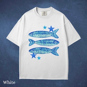 May include: White t-shirt featuring three blue fish and blue star graphics. The shirt has a crew neck and short sleeves. The text "COMET CRUSH" is printed on the upper left of the shirt.