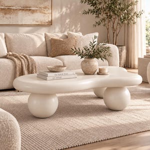 May include: A low-profile, off-white coffee table with an organic, kidney-bean-shaped top supported by three large, spherical ball legs. The surface is smooth and matte, providing a clean, sculptural base for the books and vase placed on top.
