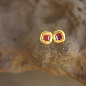 May include: A pair of gold earrings with small red square gemstones.