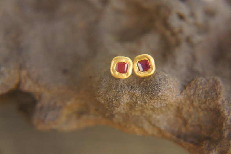 May include: A pair of gold earrings with small red square gemstones.
