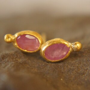 Puede incluir: Un par de pendientes de oro con piedras preciosas ovaladas de color rosa. Cada pendiente tiene una peque&ntilde;a perla dorada en el lateral.