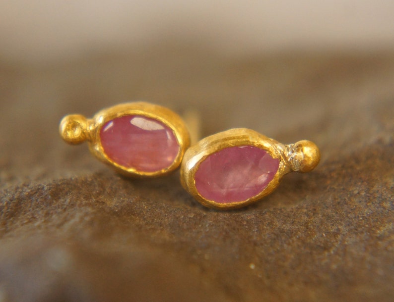 Puede incluir: Un par de pendientes de oro con piedras preciosas ovaladas de color rosa. Cada pendiente tiene una peque&ntilde;a perla dorada en el lateral.