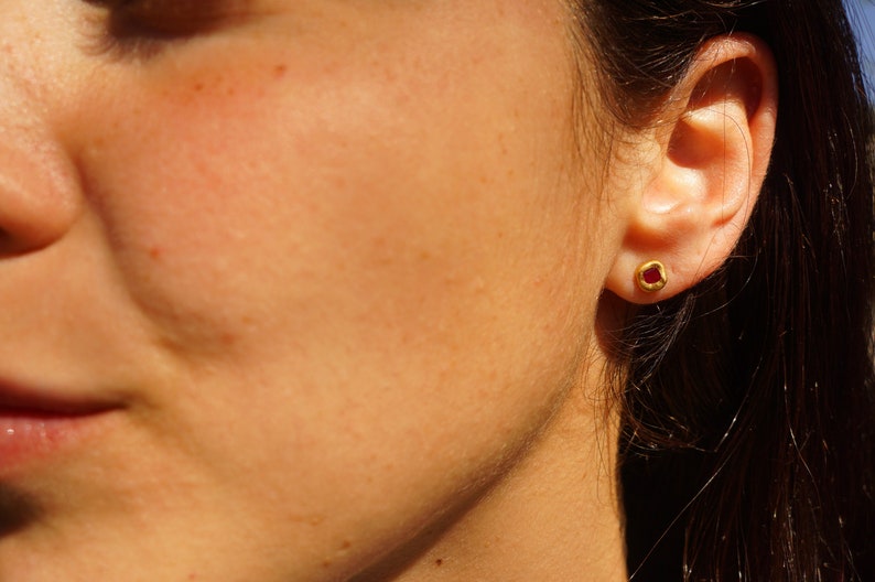 May include: A close-up of a person's ear with a small gold earring featuring a red gemstone.