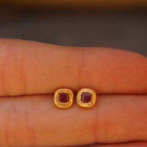 May include: A pair of gold earrings with small square red gemstones.