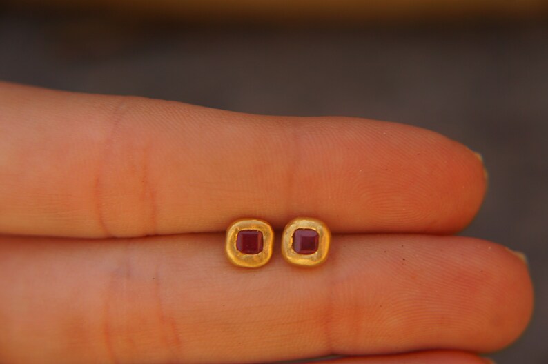 May include: A pair of gold earrings with small square red gemstones.