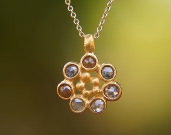 May include: A gold necklace with a pendant featuring a cluster of small, round, grey and brown diamonds set in a gold flower shape.