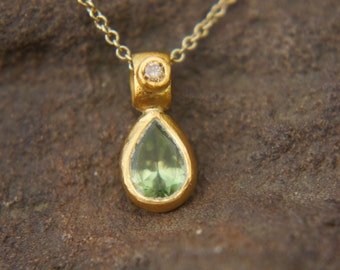 May include: A gold necklace with a teardrop-shaped pendant featuring a green gemstone and a small diamond accent.