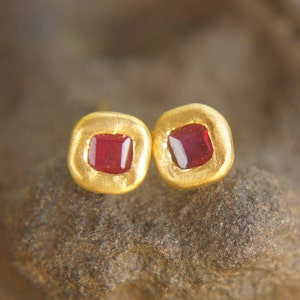 May include: A pair of gold earrings with small, square red gemstones set in the centre.
