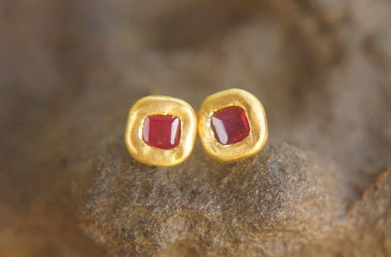 May include: A pair of gold earrings with small, square red gemstones set in the centre.