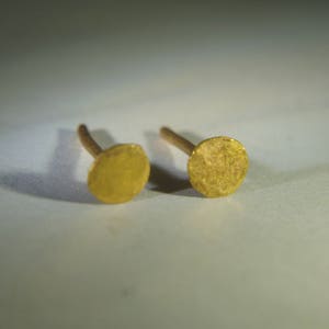 Op de afbeelding: Een paar gouden oorbel studs met een rond, getextureerd ontwerp.