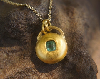 May include: A gold pendant necklace with a round, textured, gold charm featuring a green gemstone.