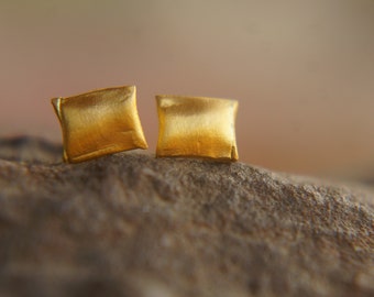 Op de afbeelding: Een paar vierkante oorbellen in goudkleur. De oorbellen zijn gemaakt van geborsteld metaal en hebben een licht getextureerd oppervlak.