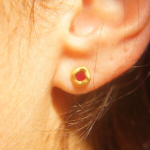 May include: A close-up of a person's ear with a small gold earring featuring a red gemstone.