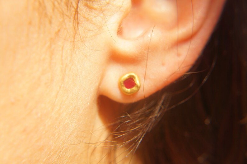 May include: A close-up of a person's ear with a small gold earring featuring a red gemstone.